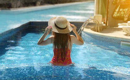 Image of Girl with straw hat in swimming pool at sea resort