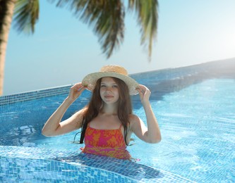 Image of Girl with straw hat in swimming pool at sea resort