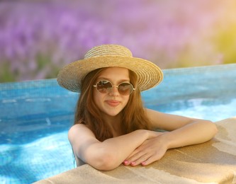 Image of Girl with straw hat and sunglasses in swimming pool at sea resort