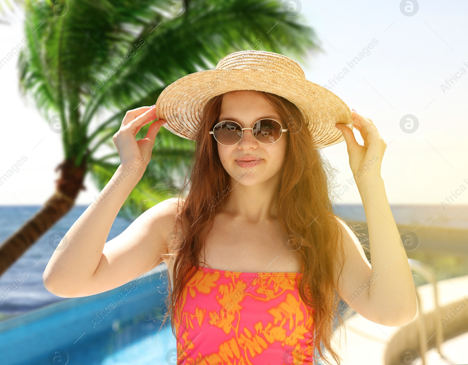 Image of Girl with straw hat and sunglasses in swimming pool at sea resort