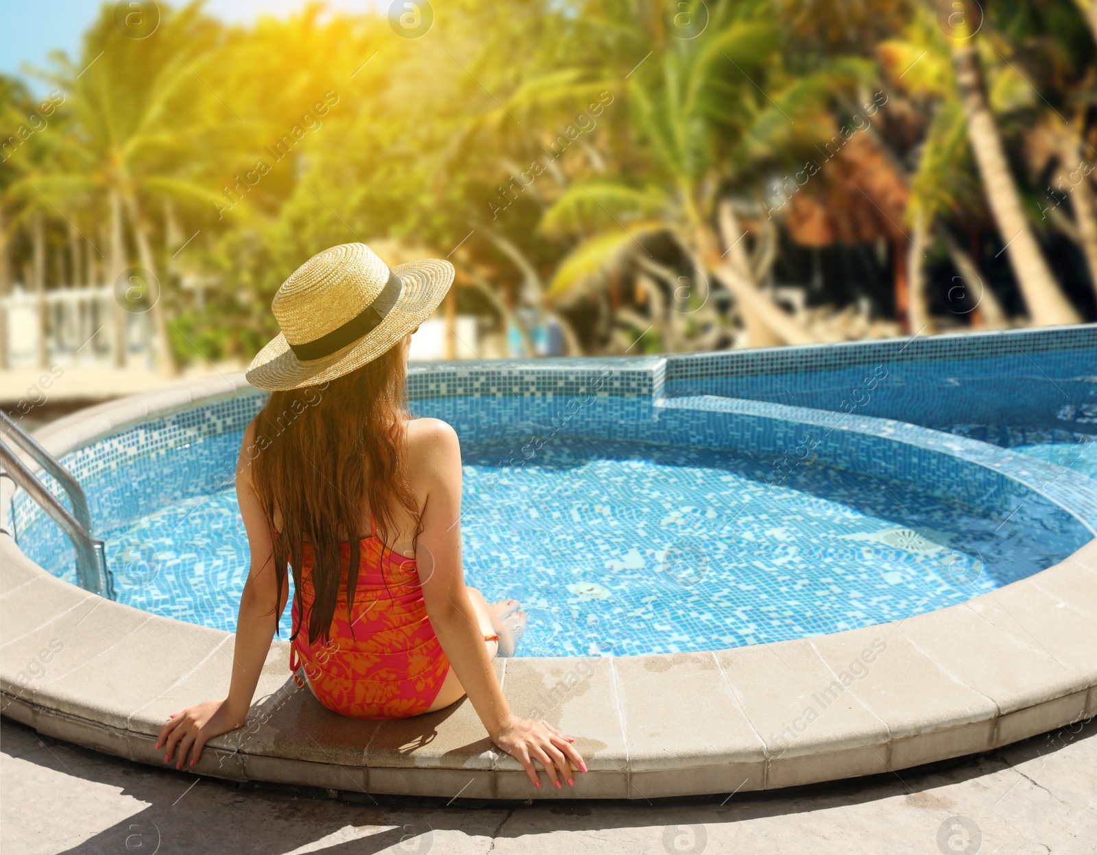 Image of Girl in straw hat sitting on edge of swimming pool at sea resort