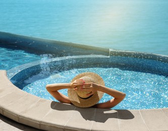 Image of Girl with straw hat resting in swimming pool at sea resort