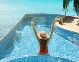 Image of Girl with straw hat in swimming pool at sea resort
