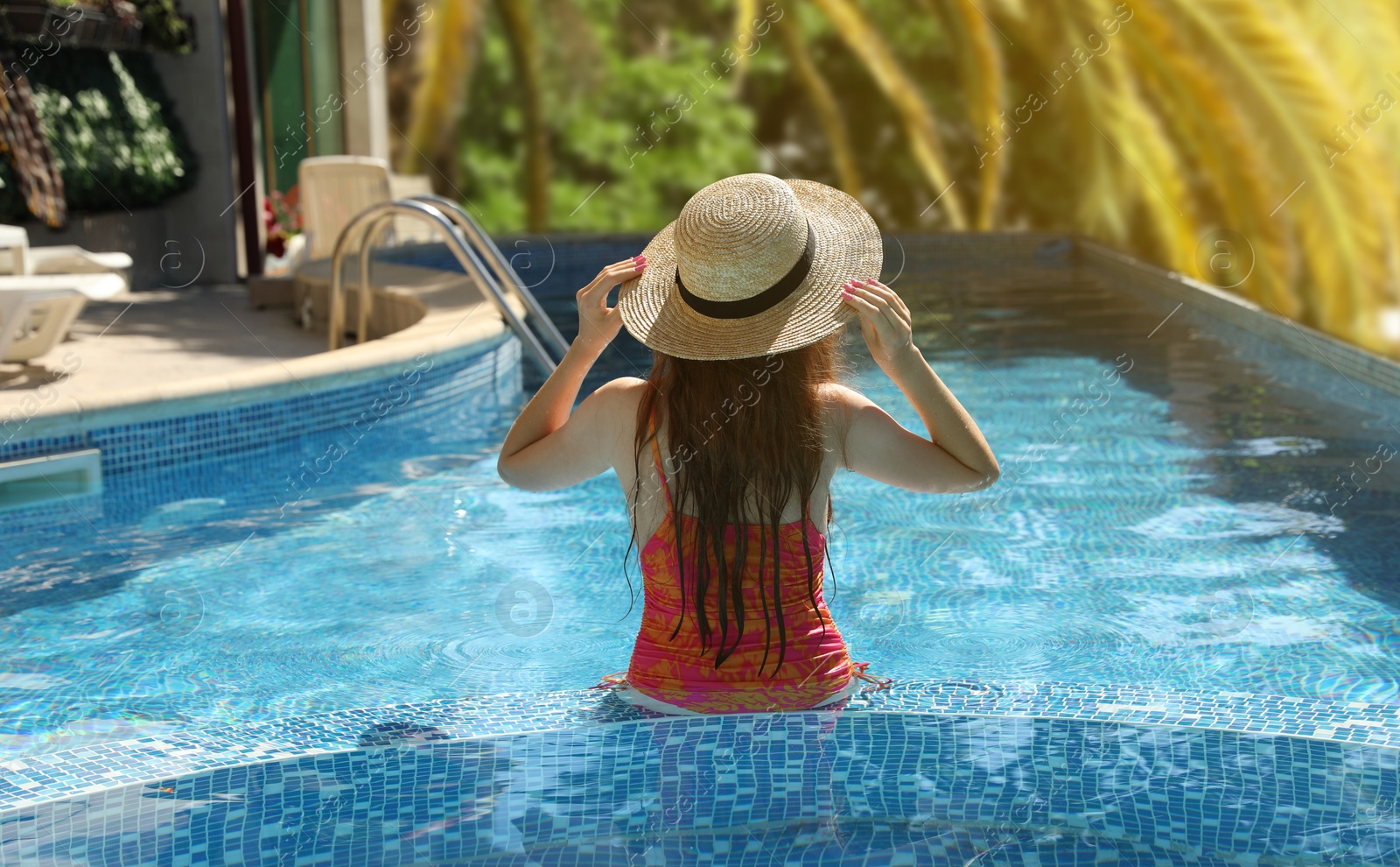 Image of Girl with straw hat in swimming pool at sea resort