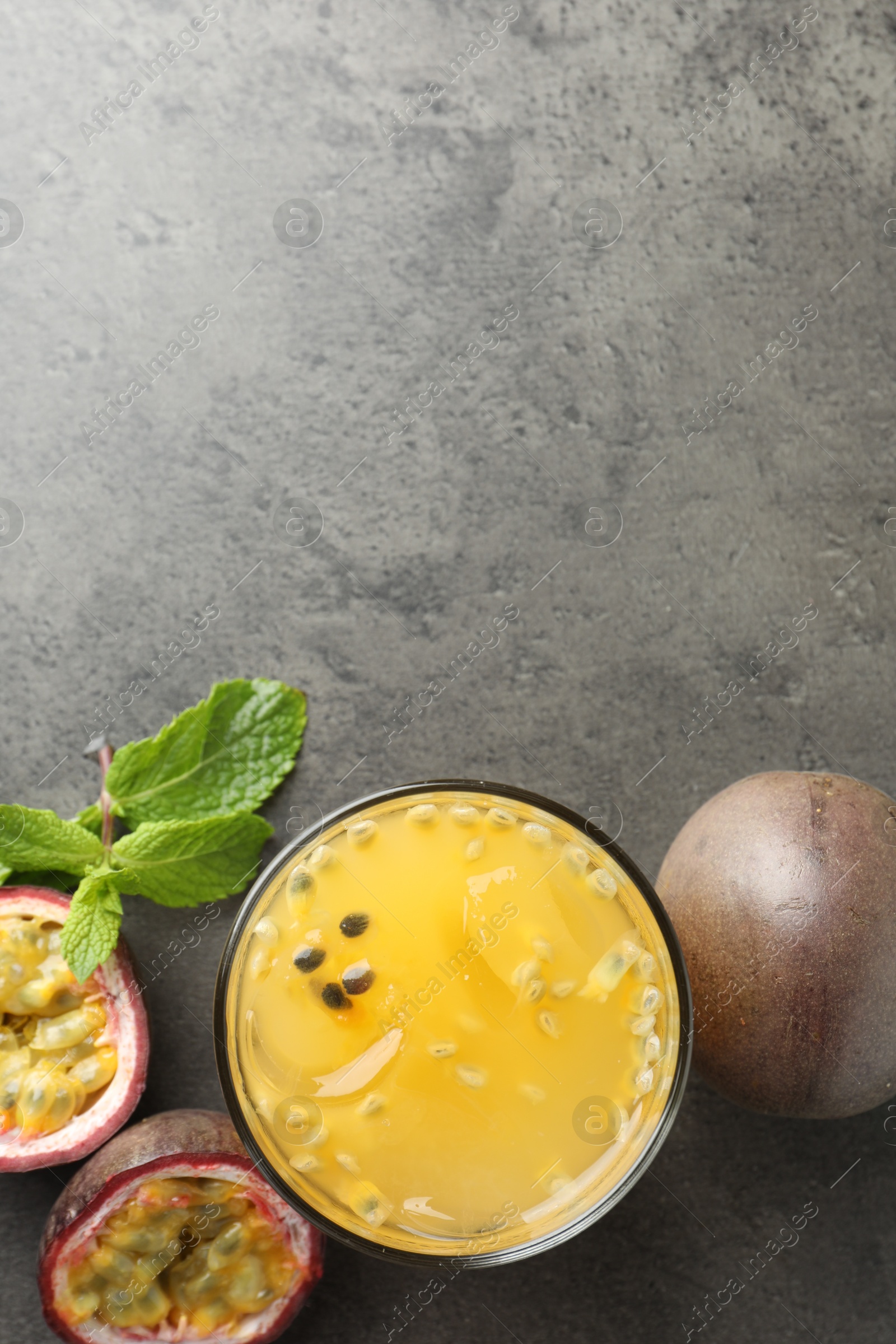 Photo of Tasty passion fruit drink with mint and fresh fruits on grey table, flat lay. Space for text
