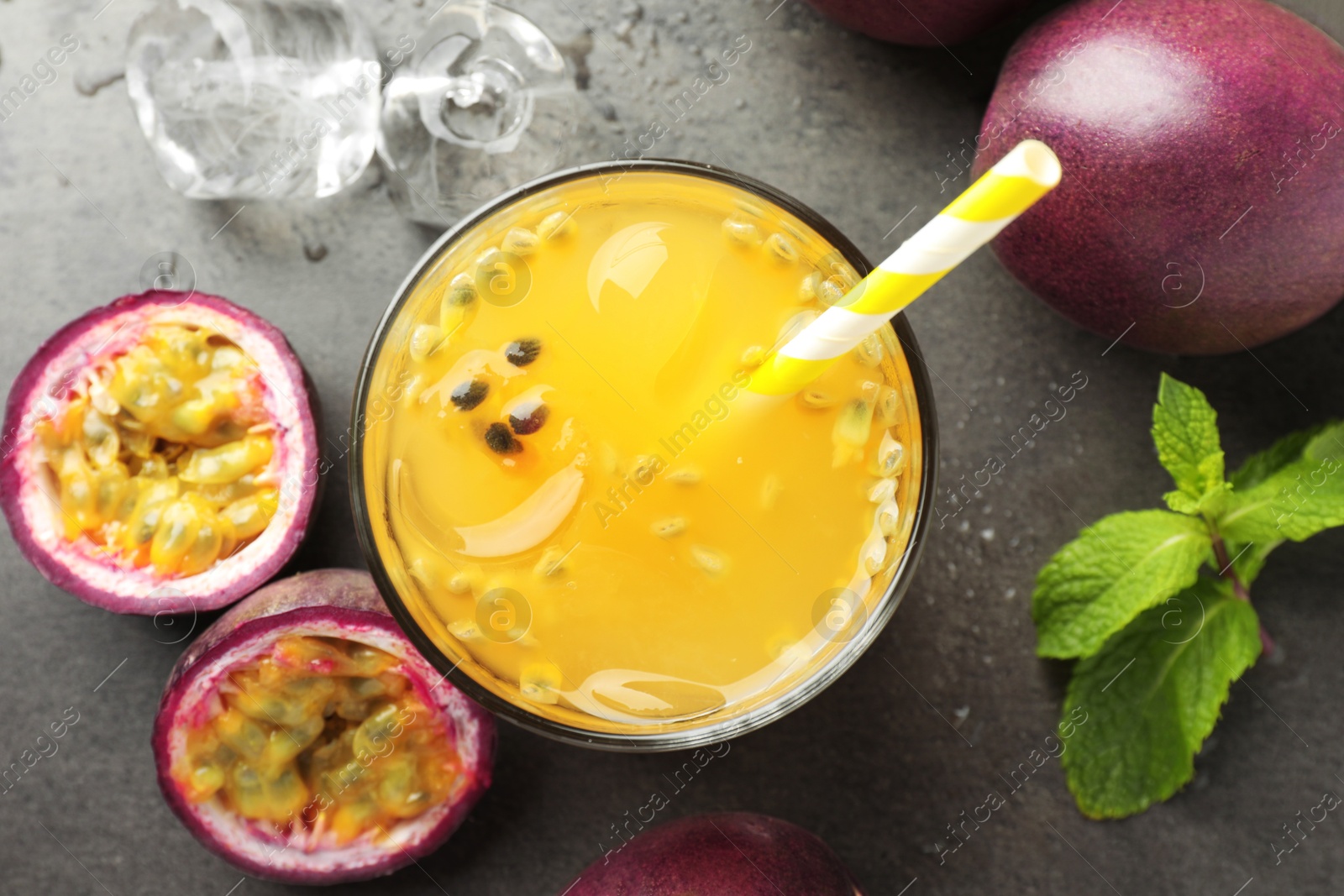 Photo of Tasty passion fruit drink with mint, ice cubes and fresh fruits on grey table, flat lay