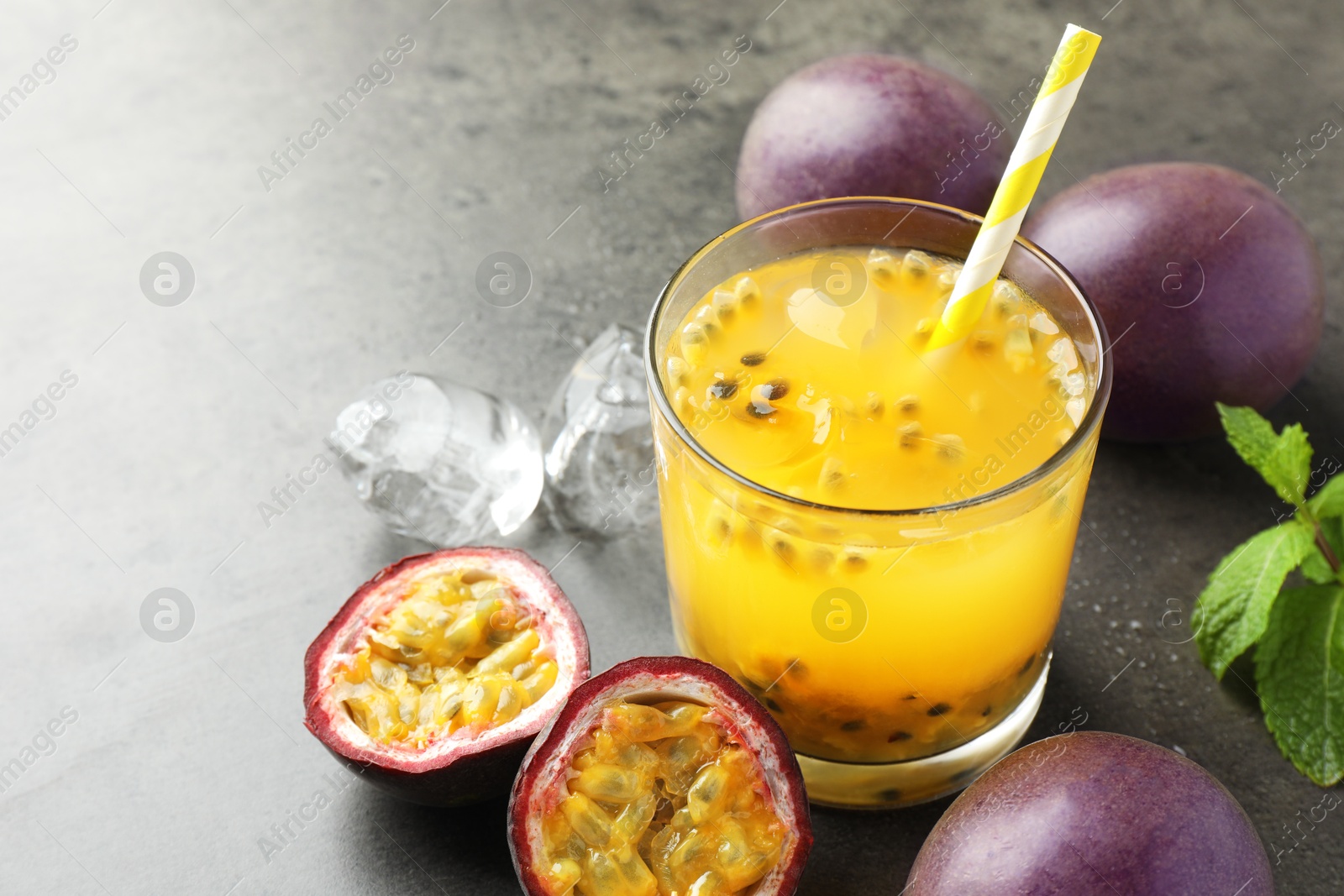 Photo of Tasty passion fruit drink with mint, ice cubes and fresh fruits on grey table, closeup. Space for text