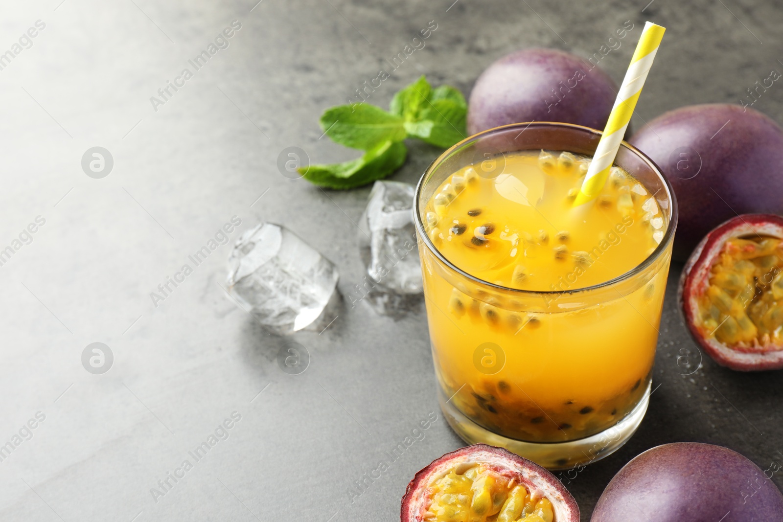 Photo of Tasty passion fruit drink with mint, ice cubes and fresh fruits on grey table, closeup. Space for text