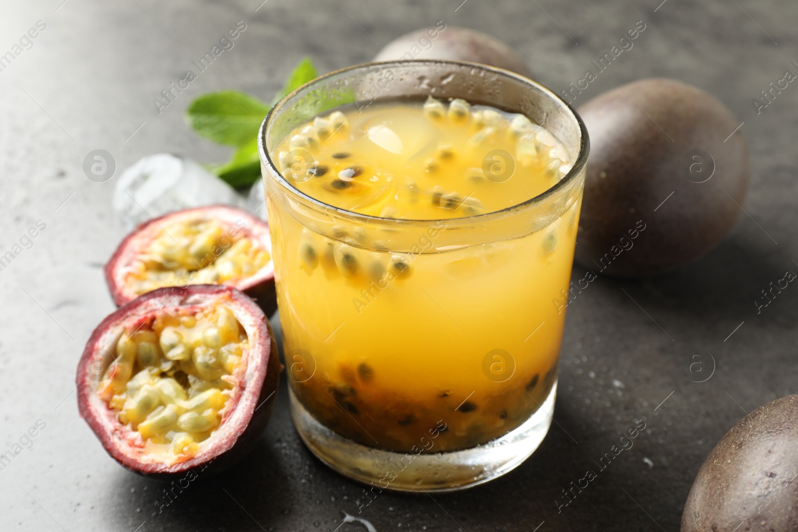 Photo of Tasty passion fruit drink with mint, ice cubes and fresh fruits on grey table, closeup