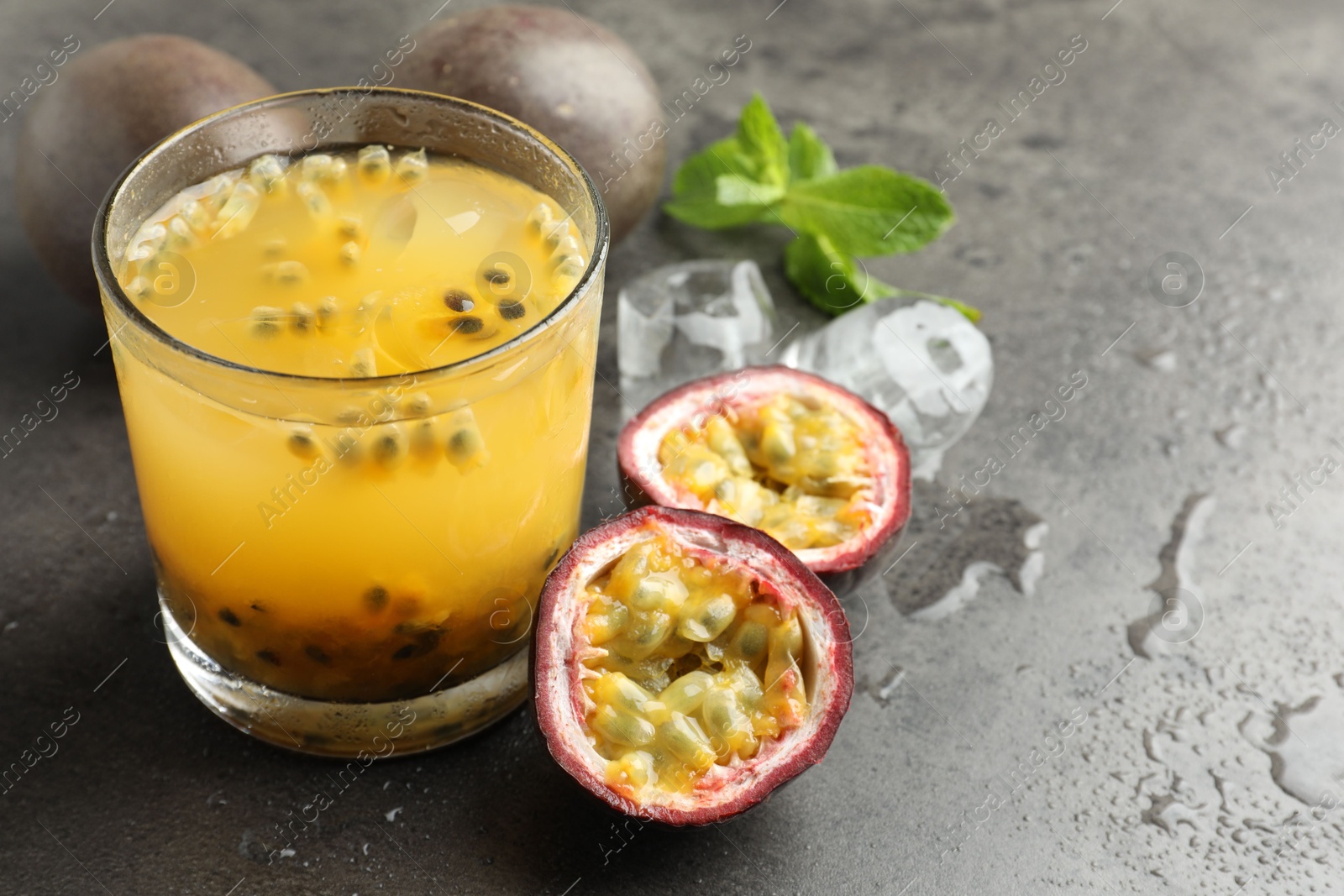 Photo of Tasty passion fruit drink with mint, ice cubes and fresh fruits on grey table, closeup. Space for text