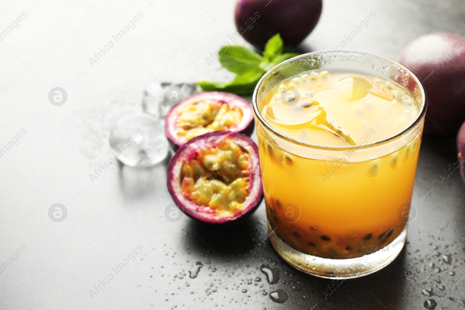 Photo of Tasty passion fruit drink with mint, ice cubes and fresh fruits on grey table, closeup. Space for text