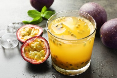 Photo of Tasty passion fruit drink with mint, ice cubes and fresh fruits on grey table, closeup