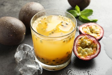Photo of Tasty passion fruit drink with mint, ice cubes and fresh fruits on grey table, closeup