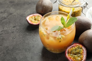 Photo of Tasty passion fruit drink with mint and fresh fruits on grey table, closeup. Space for text