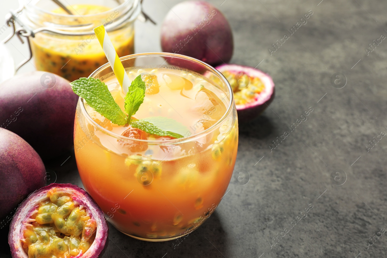 Photo of Tasty passion fruit drink with mint and fresh fruits on grey table, closeup. Space for text