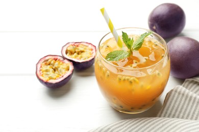 Photo of Tasty passion fruit drink with mint and fresh fruits on white wooden table, closeup
