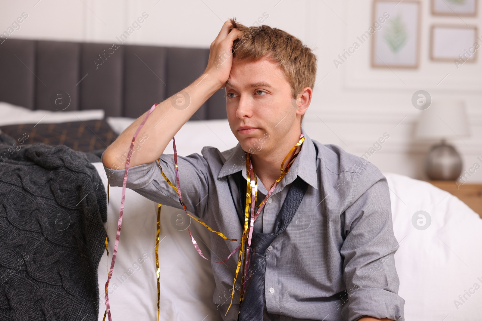 Photo of Man with streamers suffering from hangover near bed indoors