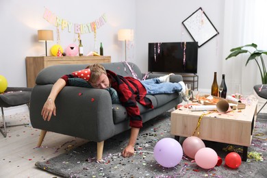 Photo of Man suffering from hangover on sofa in messy room after party