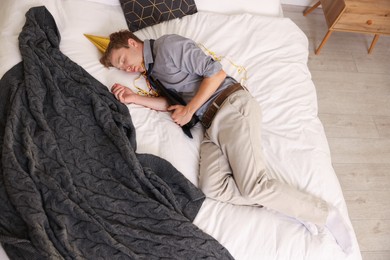 Photo of Man with bottle of alcohol suffering from hangover on bed indoors, above view
