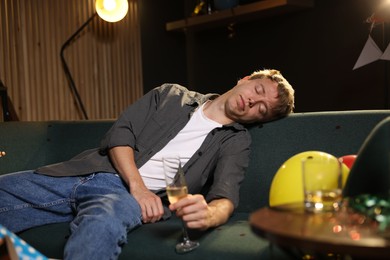 Photo of Man with glass of alcohol suffering from hangover on sofa in messy room after party