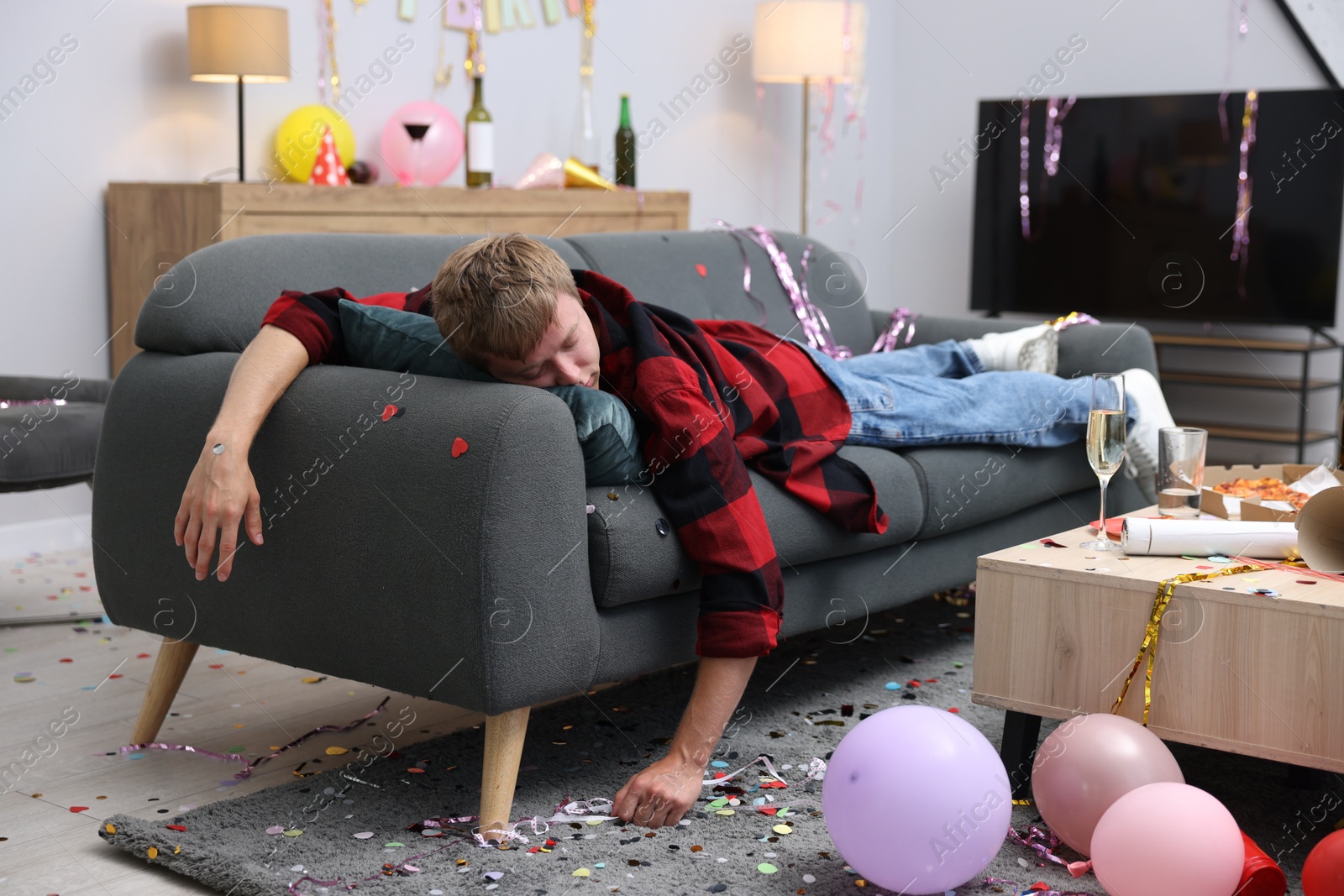 Man suffering from hangover on sofa in messy room after party Photo of Man suffering from hangover on sofa in messy room after party