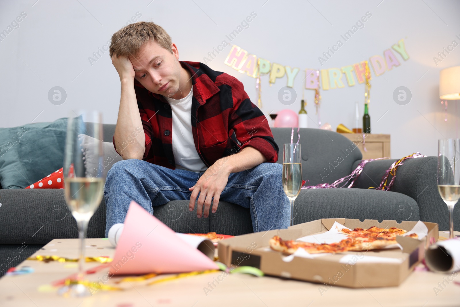Man suffering from hangover on sofa in messy room after party Photo of Man suffering from hangover on sofa in messy room after party