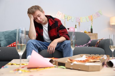 Photo of Man suffering from hangover on sofa in messy room after party