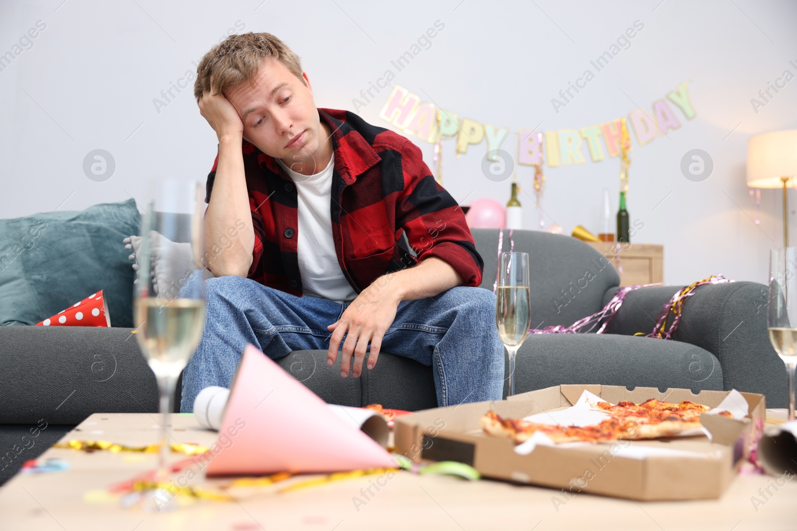 Man suffering from hangover on sofa in messy room after party Photo of Man suffering from hangover on sofa in messy room after party