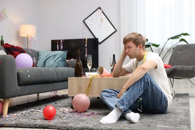 Photo of Man suffering from hangover on floor in messy room after party