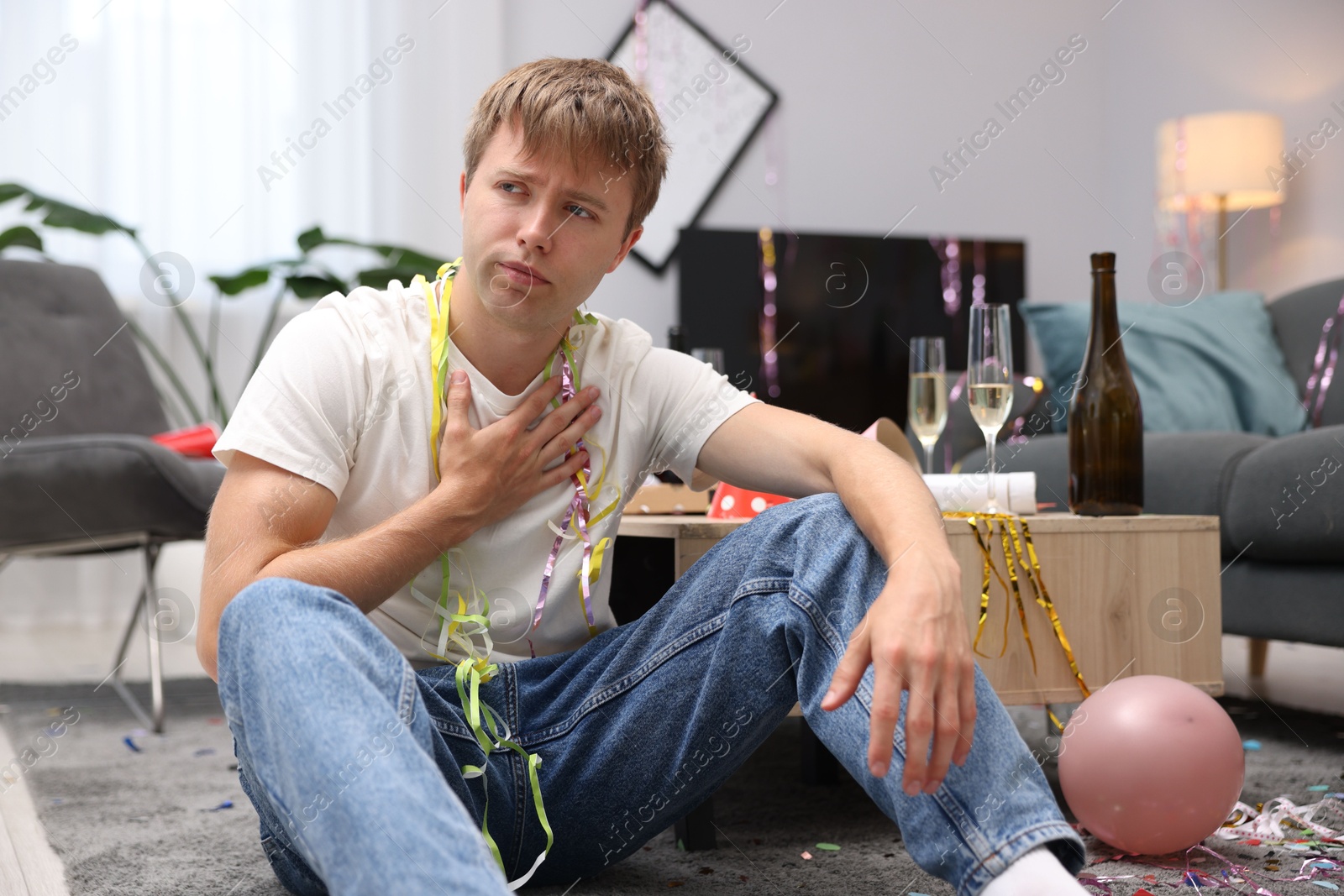 Man suffering from hangover on floor in messy room after party Photo of Man suffering from hangover on floor in messy room after party