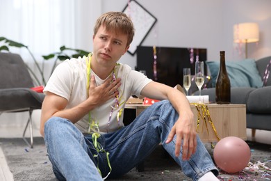 Photo of Man suffering from hangover on floor in messy room after party
