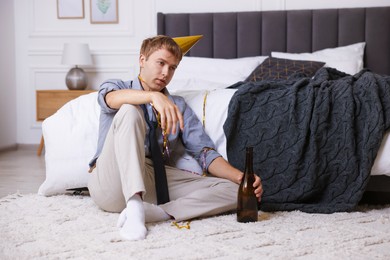Photo of Man with alcohol suffering from hangover near bed indoors