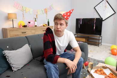 Photo of Man suffering from hangover on sofa in messy room after party