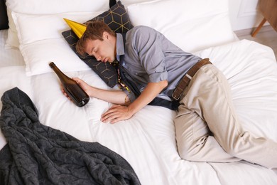 Photo of Man with alcohol suffering from hangover on bed indoors, above view