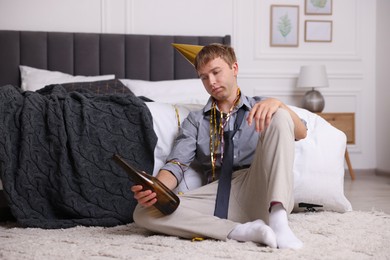 Photo of Man with bottle of alcohol suffering from hangover near bed indoors