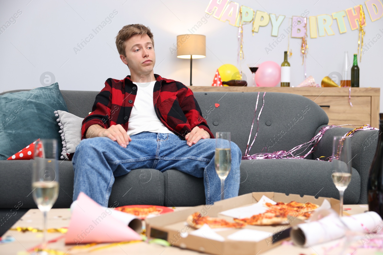 Man suffering from hangover on sofa in messy room after party Photo of Man suffering from hangover on sofa in messy room after party