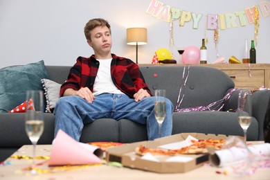 Photo of Man suffering from hangover on sofa in messy room after party