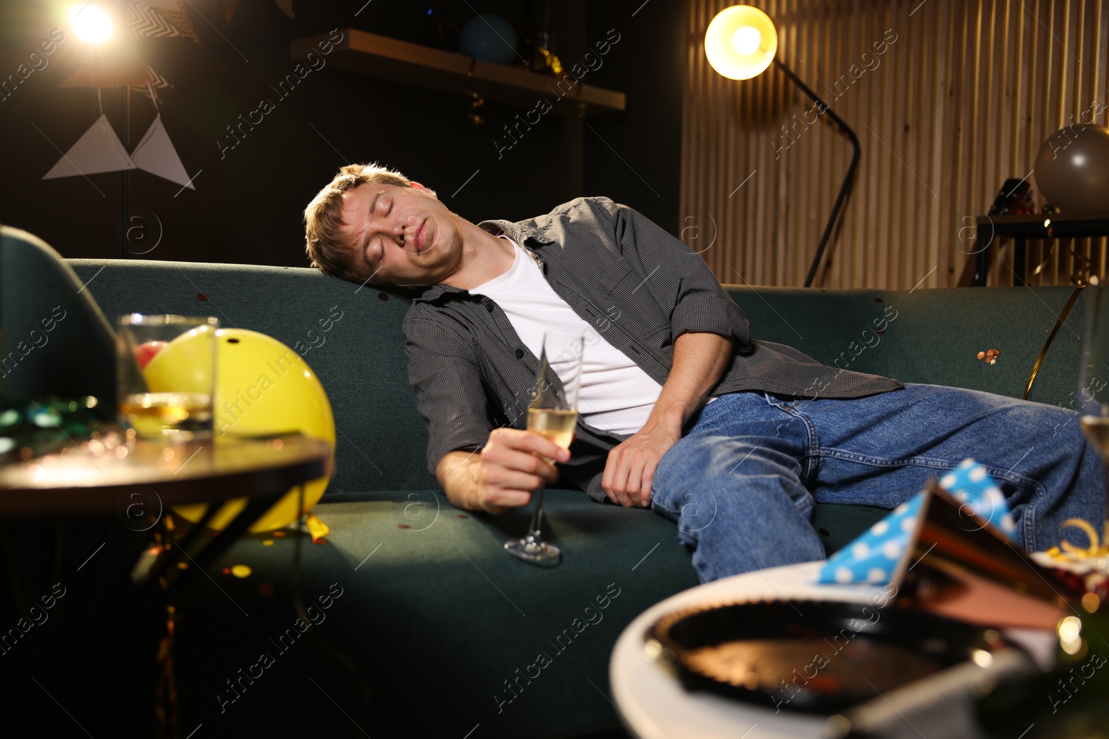 Man with glass of alcohol suffering from hangover on sofa in messy room after party Photo of Man with glass of alcohol suffering from hangover on sofa in messy room after party