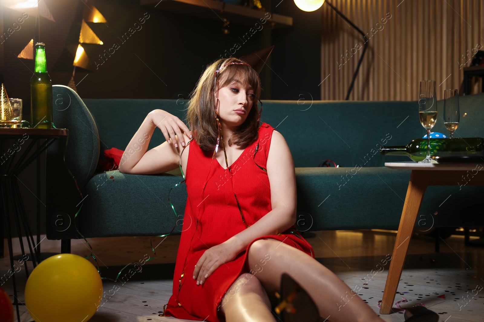 Woman suffering from hangover near sofa in messy room after party Photo of Woman suffering from hangover near sofa in messy room after party