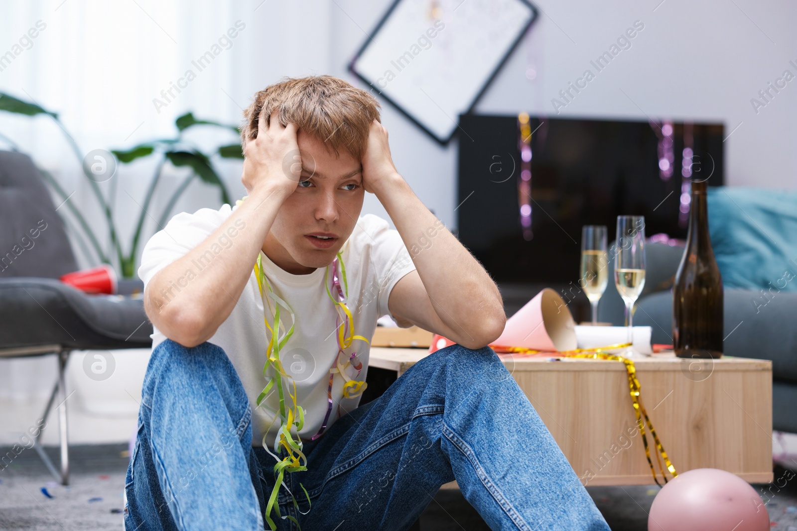 Man suffering from hangover on floor in messy room after party Photo of Man suffering from hangover on floor in messy room after party