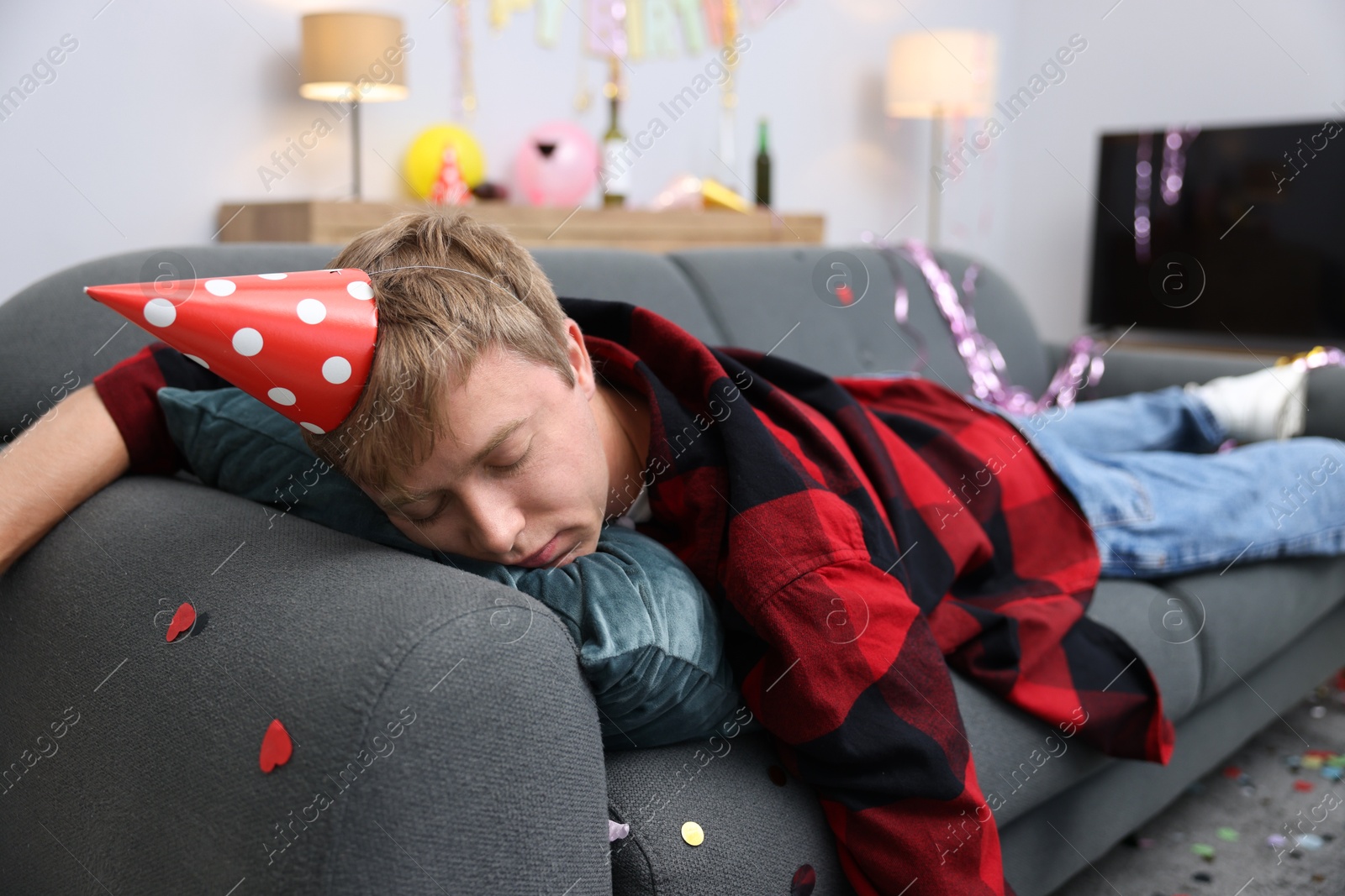Man suffering from hangover on sofa in messy room after party Photo of Man suffering from hangover on sofa in messy room after party