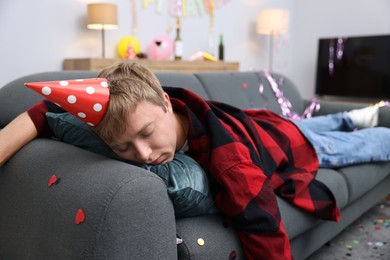Photo of Man suffering from hangover on sofa in messy room after party