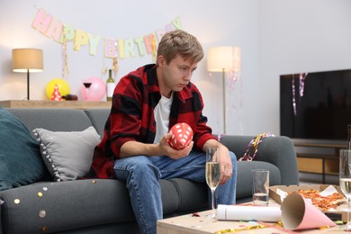 Photo of Man suffering from hangover on sofa in messy room after party