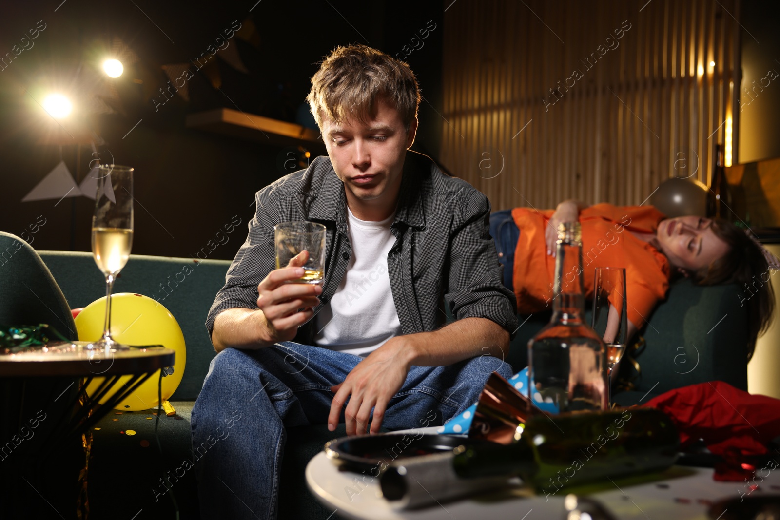 Photo of Man with glass of alcohol suffering from hangover on sofa in messy room after party