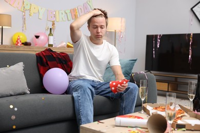 Photo of Man suffering from hangover on sofa in messy room after party