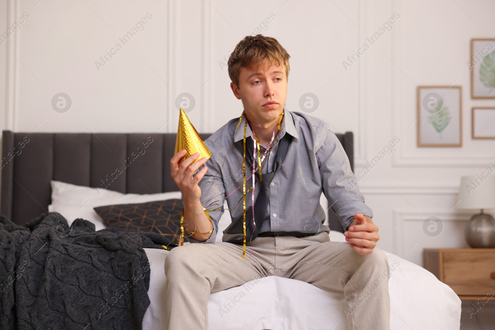 Man with party hat suffering from hangover on bed indoors Photo of Man with party hat suffering from hangover on bed indoors