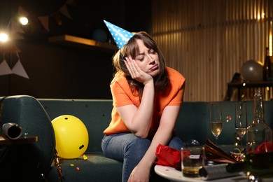 Photo of Woman suffering from hangover on sofa in messy room after party