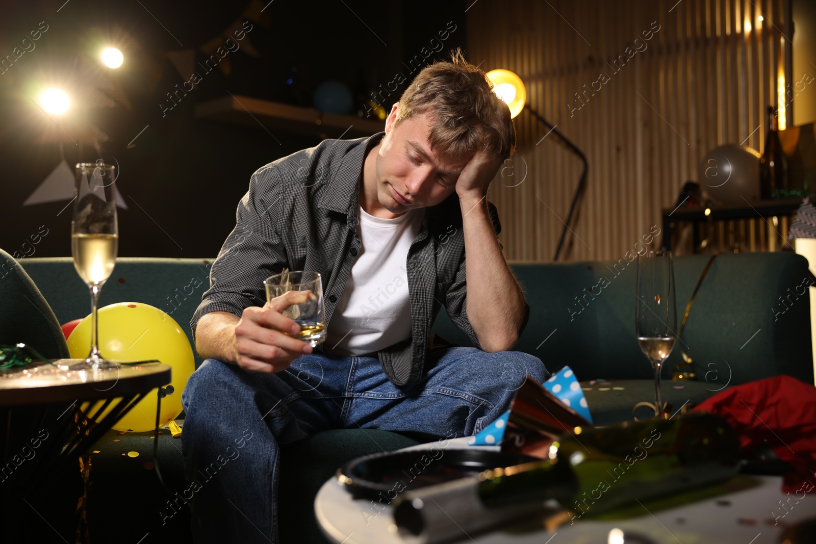 Man with glass of alcohol suffering from hangover on sofa in messy room after party Photo of Man with glass of alcohol suffering from hangover on sofa in messy room after party
