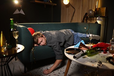 Photo of Man suffering from hangover on sofa in messy room after party