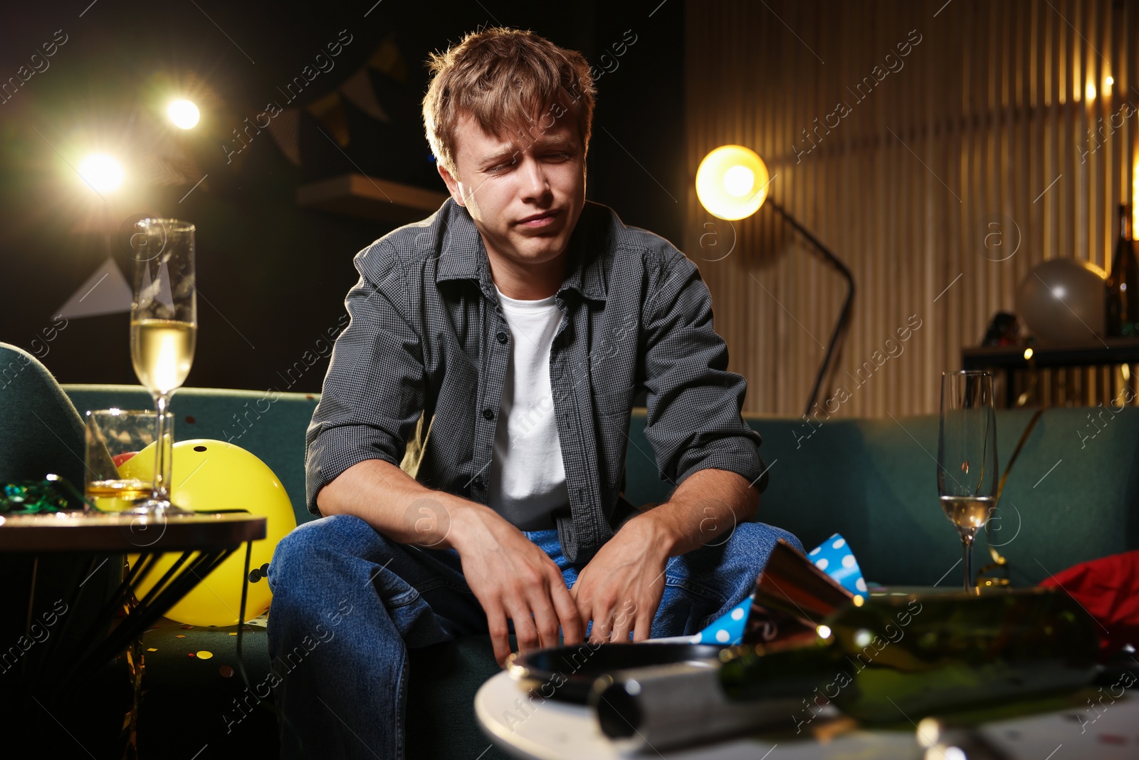 Man suffering from hangover on sofa in messy room after party Photo of Man suffering from hangover on sofa in messy room after party